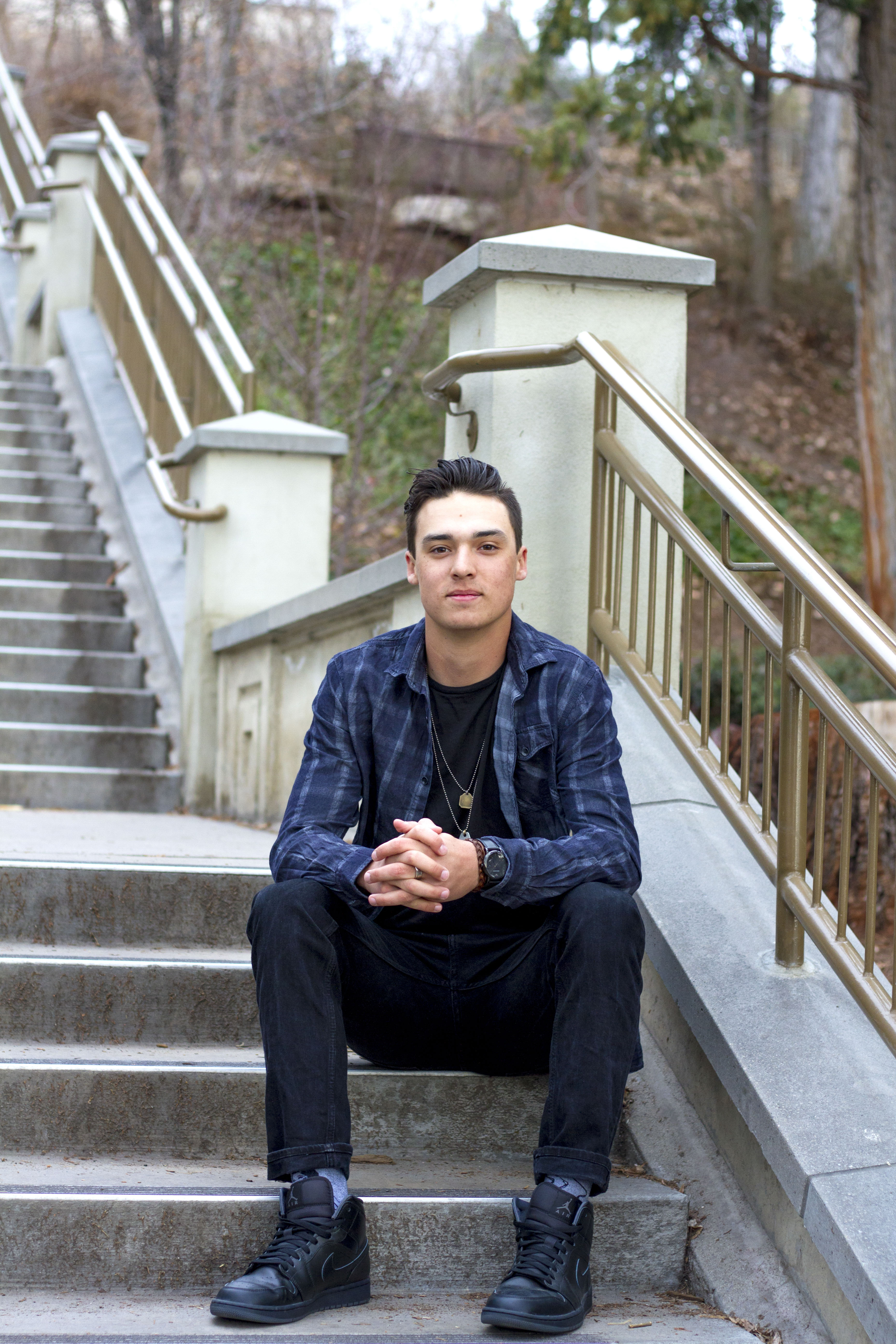 A high school senior sits on a long outdoor staircase at BYU for his graduation photos.