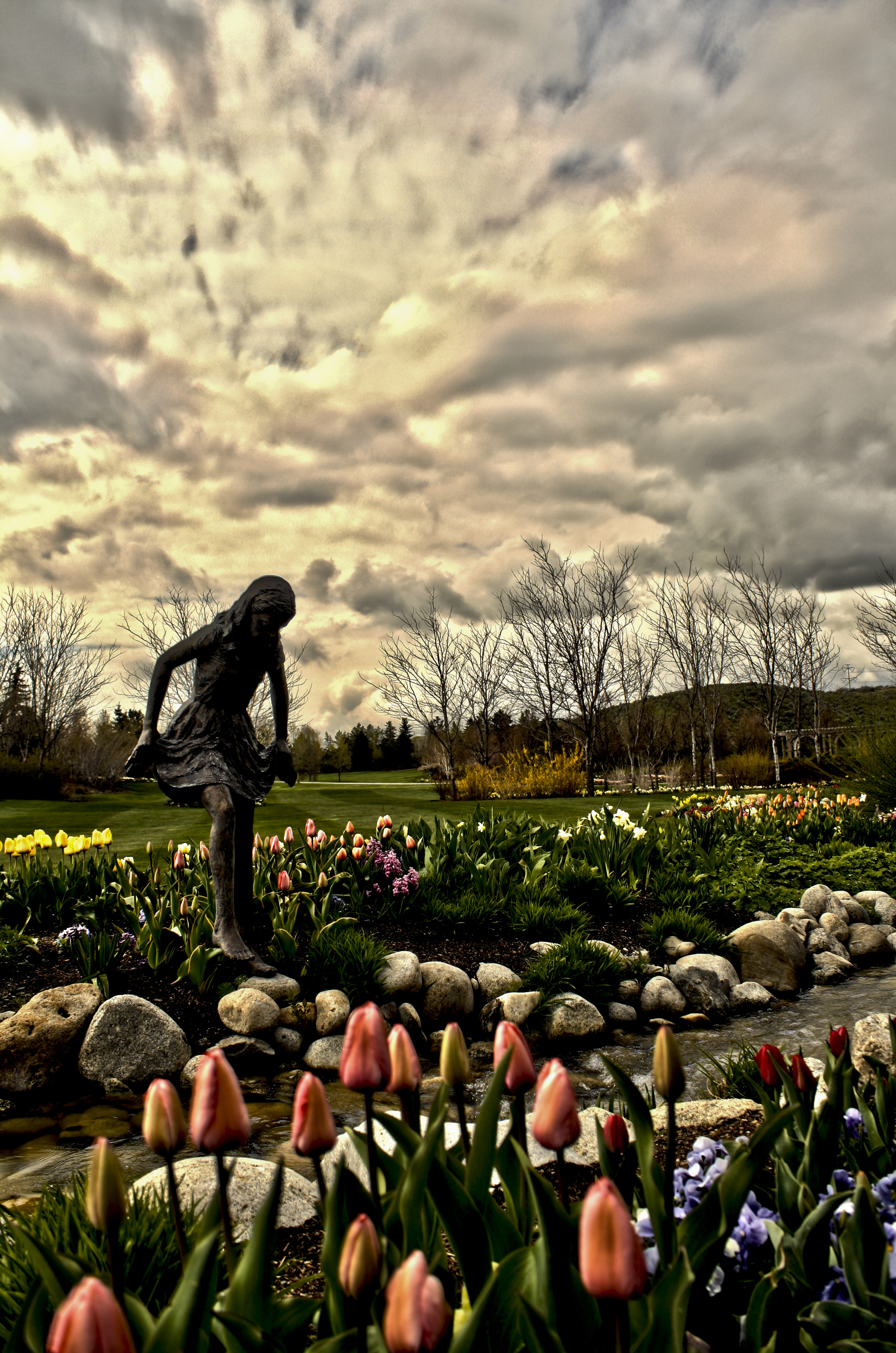 A classical statue surrounded by vibrant pink and purple flowers in a garden.