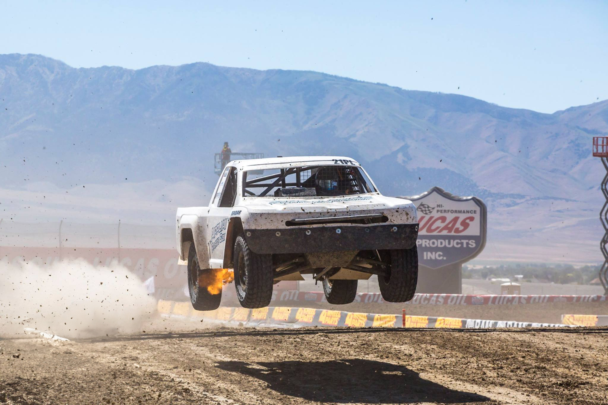 An off-road truck with a red and yellow fire-themed design racing on a dirt track.