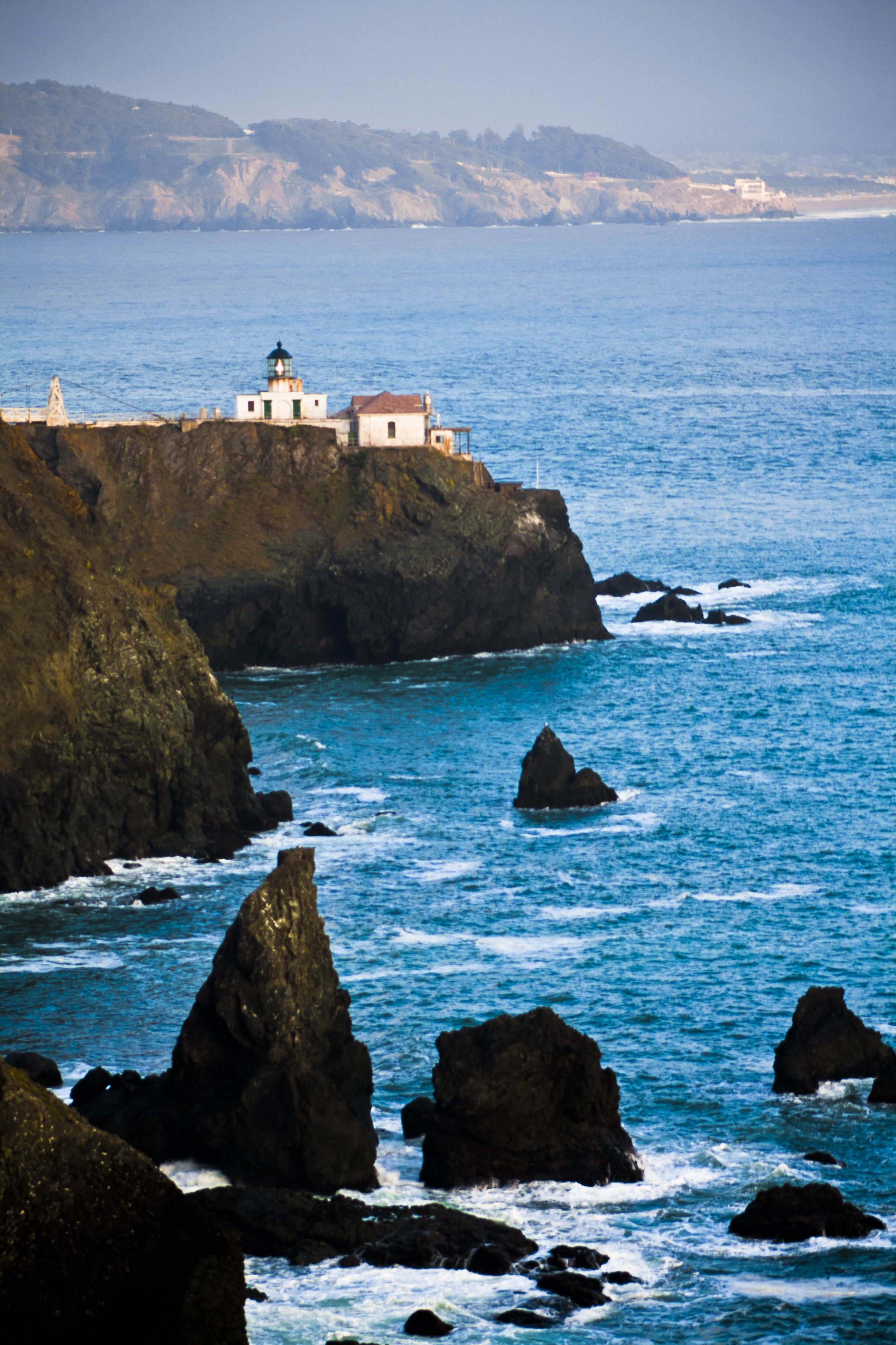 A tall white lighthouse on a rocky coast under a cloudy sky.